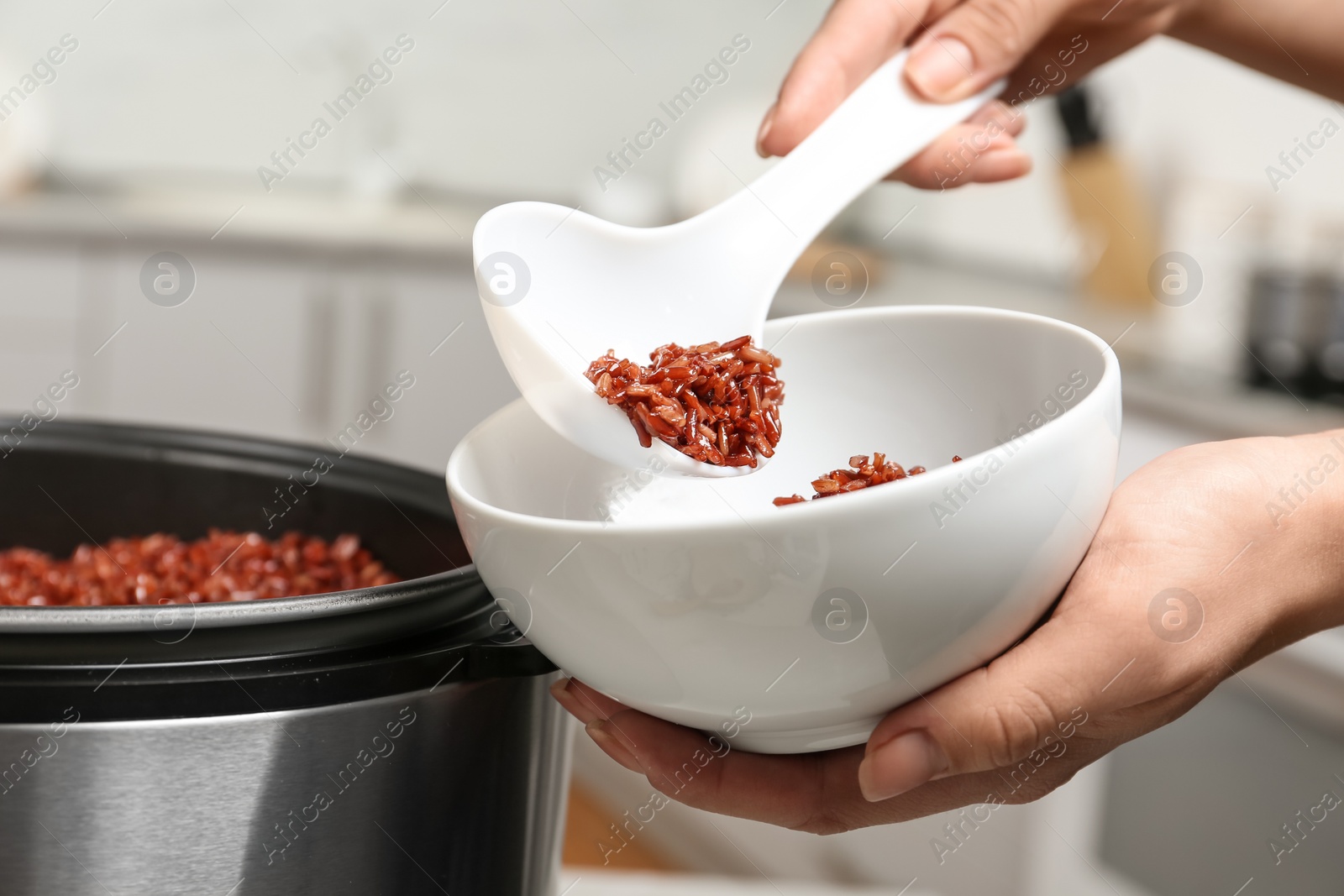 Photo of Woman putting brown rice into bowl from multi cooker in kitchen, closeup