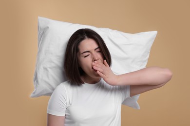 Photo of Sleepy young woman with pillow yawning on beige background. Insomnia problem