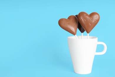 Chocolate heart shaped lollipops in cup on turquoise background. Space for text