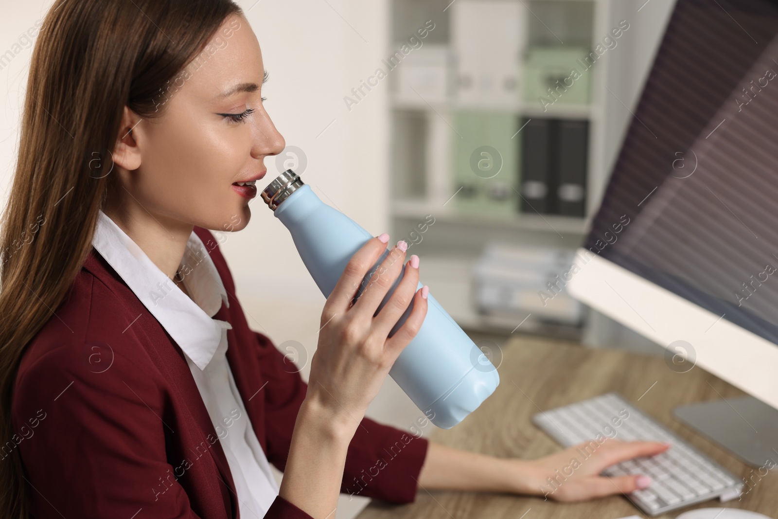 Photo of Woman holding light blue thermos bottle at workplace