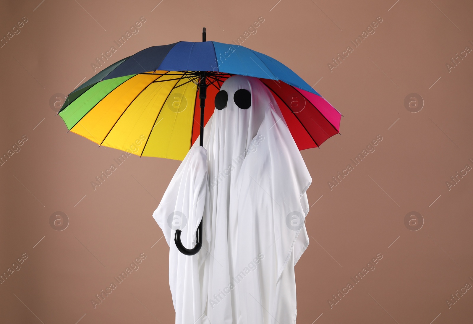 Photo of Person in ghost costume with rainbow umbrella on dark beige background