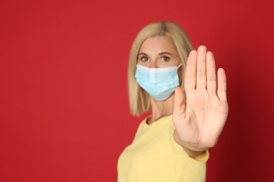 Photo of Woman in protective mask showing stop gesture on red background, space for text. Prevent spreading of coronavirus