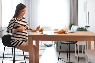 Photo of Young pregnant woman eating vegetable salad at table in kitchen