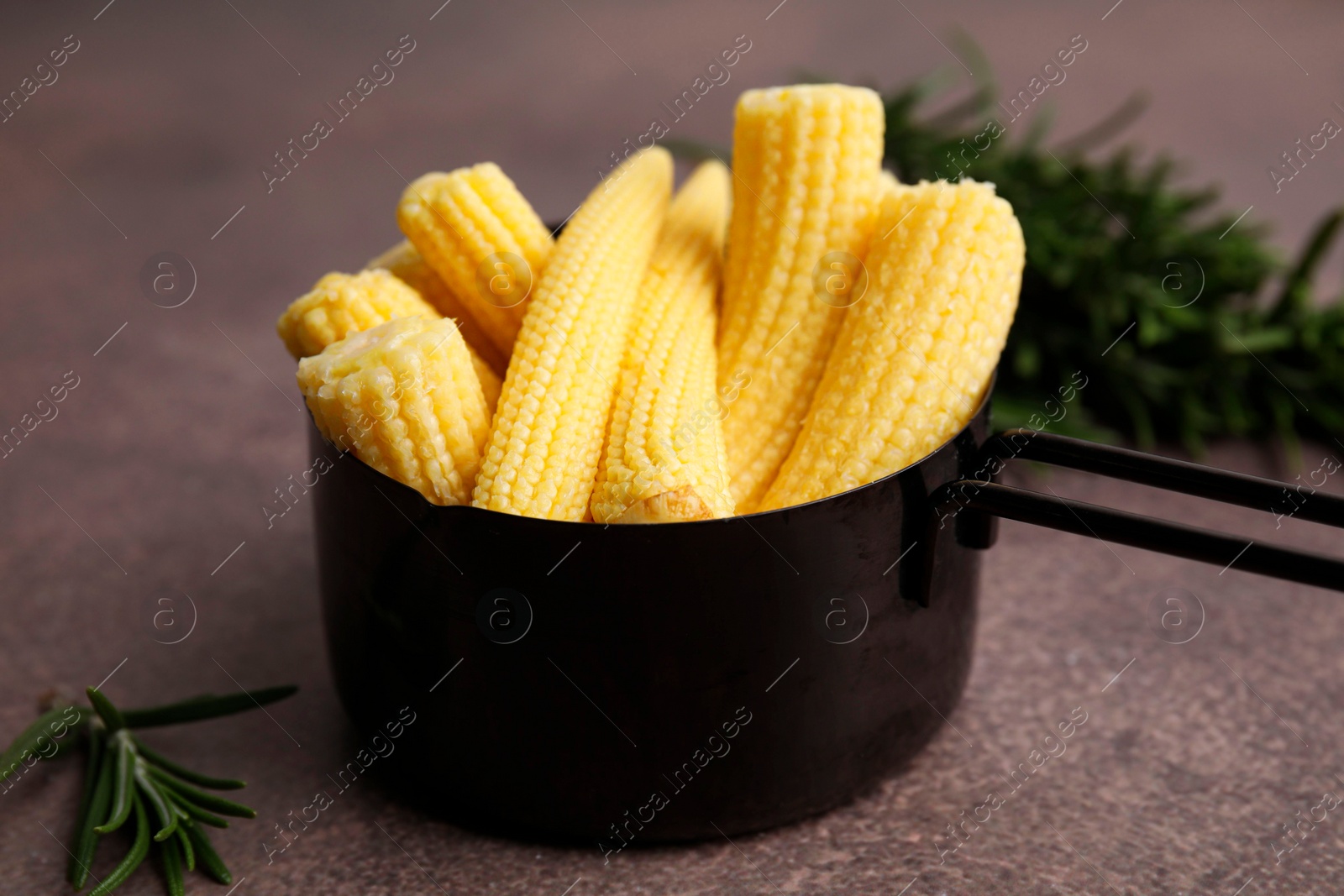 Photo of Tasty fresh yellow baby corns in dish on brown table, closeup