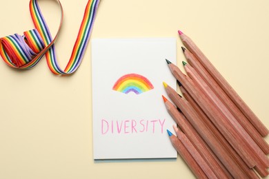 Photo of Paper sheet with word Diversity and rainbow, pencils, ribbon on beige background, flat lay