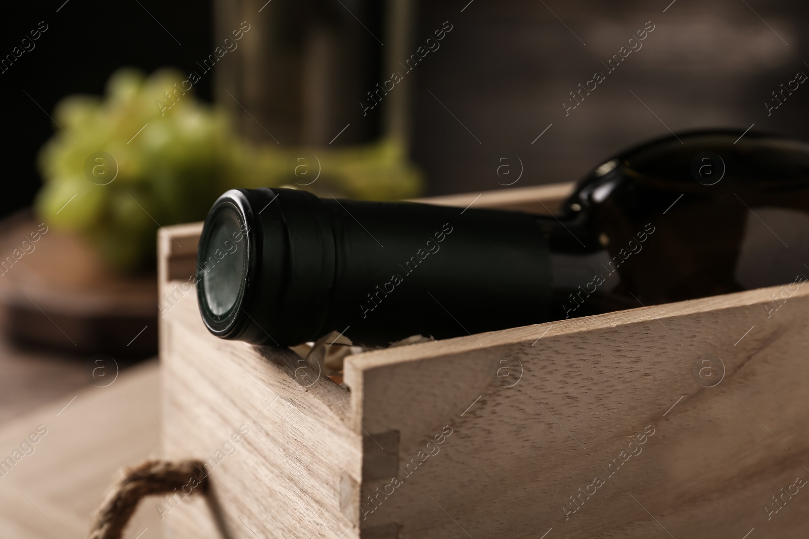 Photo of Open wooden crate with bottle of wine on blurred background