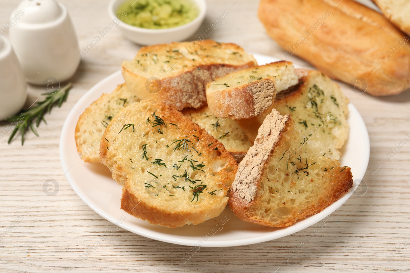 Photo of Tasty baguette with garlic, dill and rosemary on white wooden table