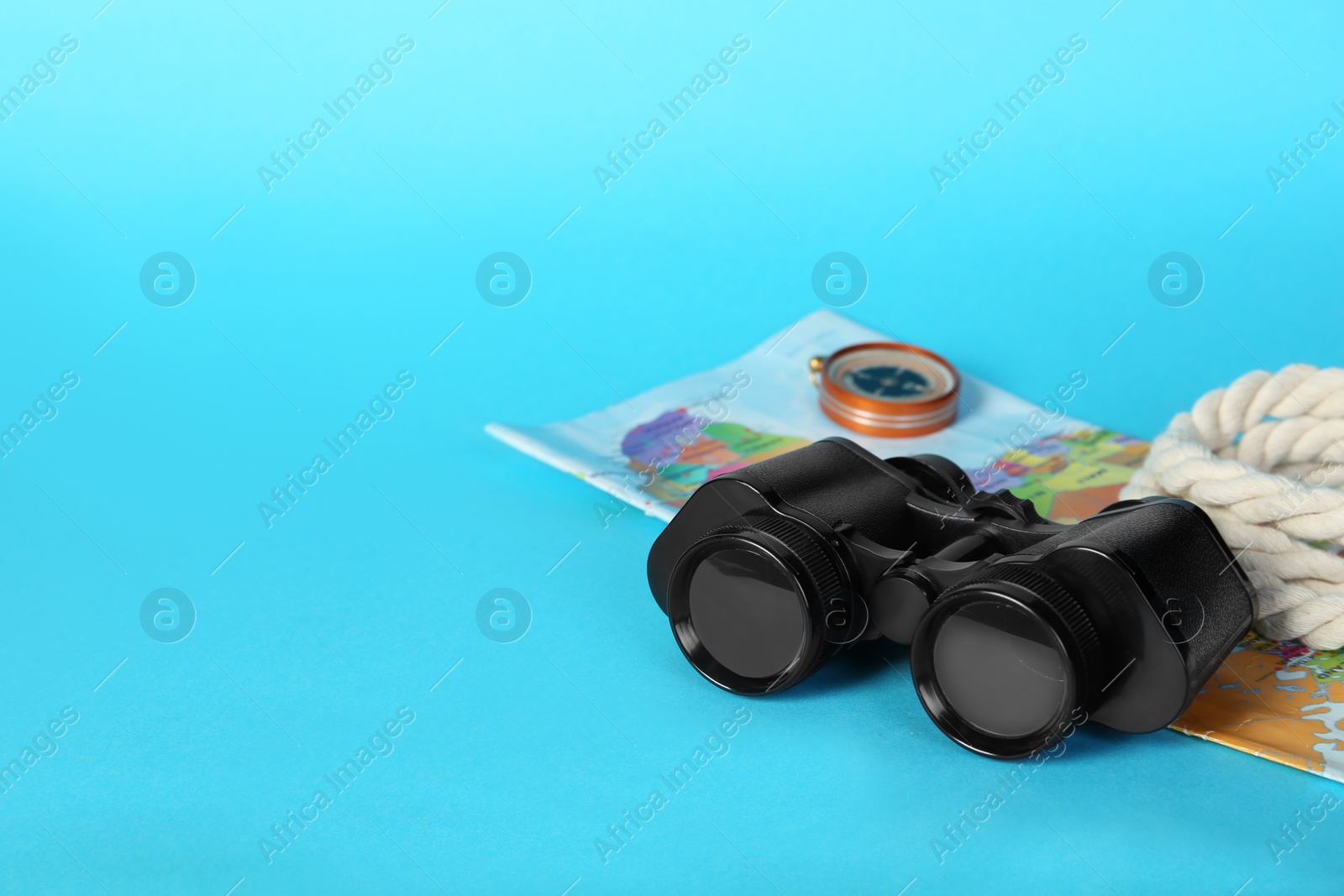 Photo of Modern binoculars, rope, map and compass on light blue background, space for text