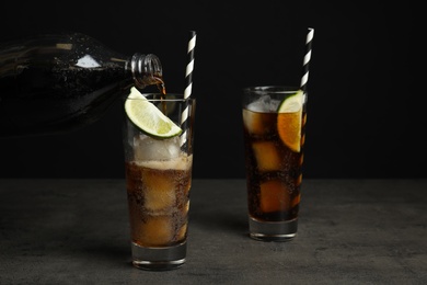 Photo of Pouring refreshing soda drink into glass on grey table against black background