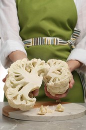 Photo of Woman holding halves of fresh cauliflower at light grey table, closeup