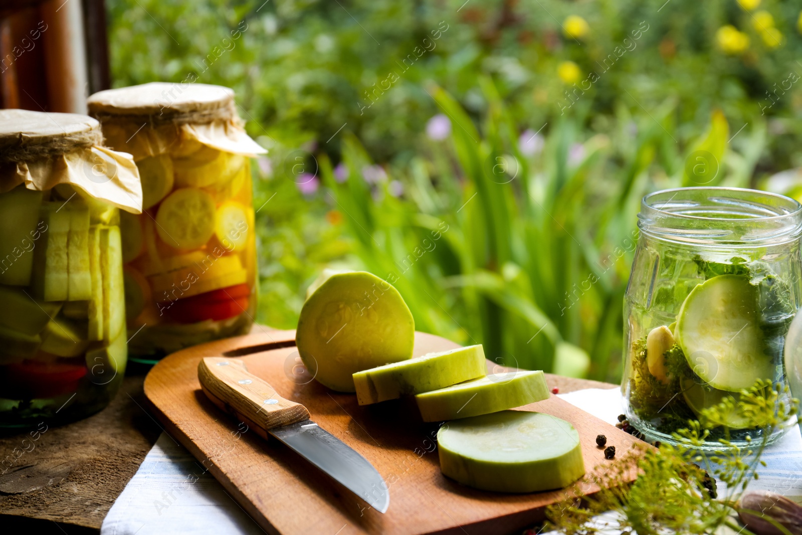 Photo of Cut fresh zucchini and jars of pickled vegetables on wooden table