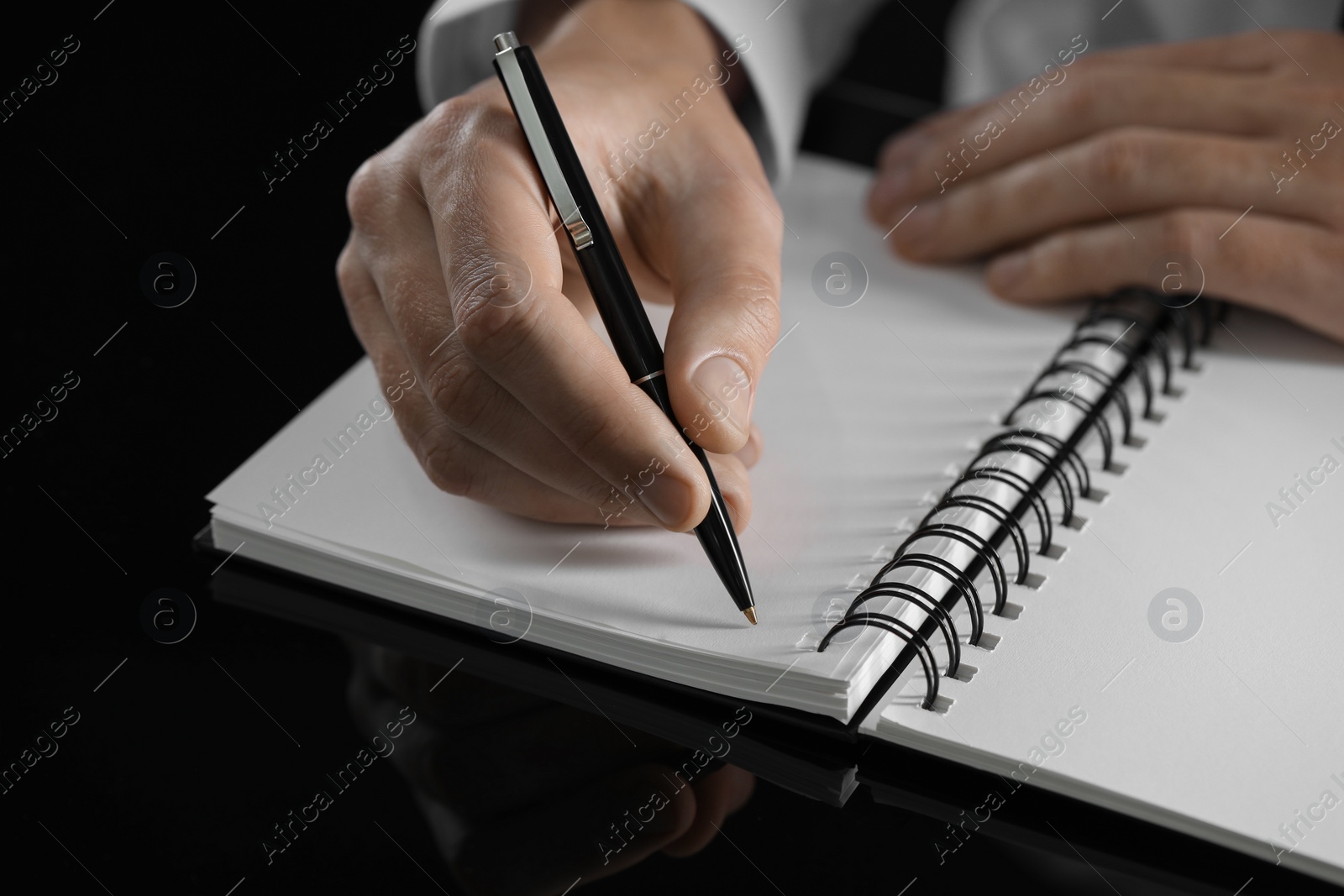 Photo of Man writing in notebook at black table, closeup