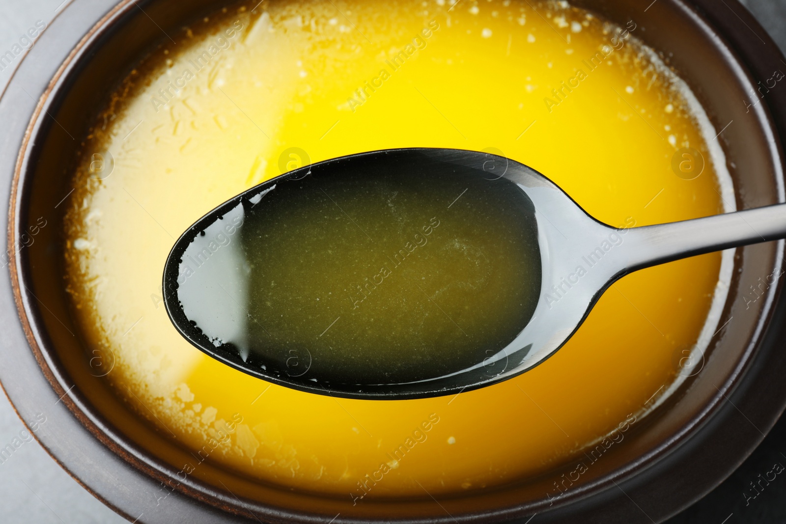 Photo of Spoon of clarified butter over bowl, closeup