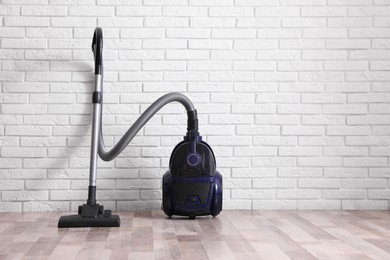 Photo of Modern vacuum cleaner near white brick wall indoors