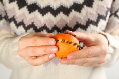 Photo of Woman decorating fresh tangerine with cloves, closeup. Making Christmas pomander ball