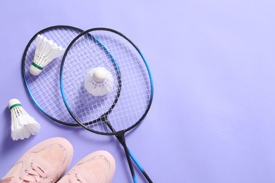 Feather badminton shuttlecocks, rackets and sneakers on violet background, flat lay. Space for text