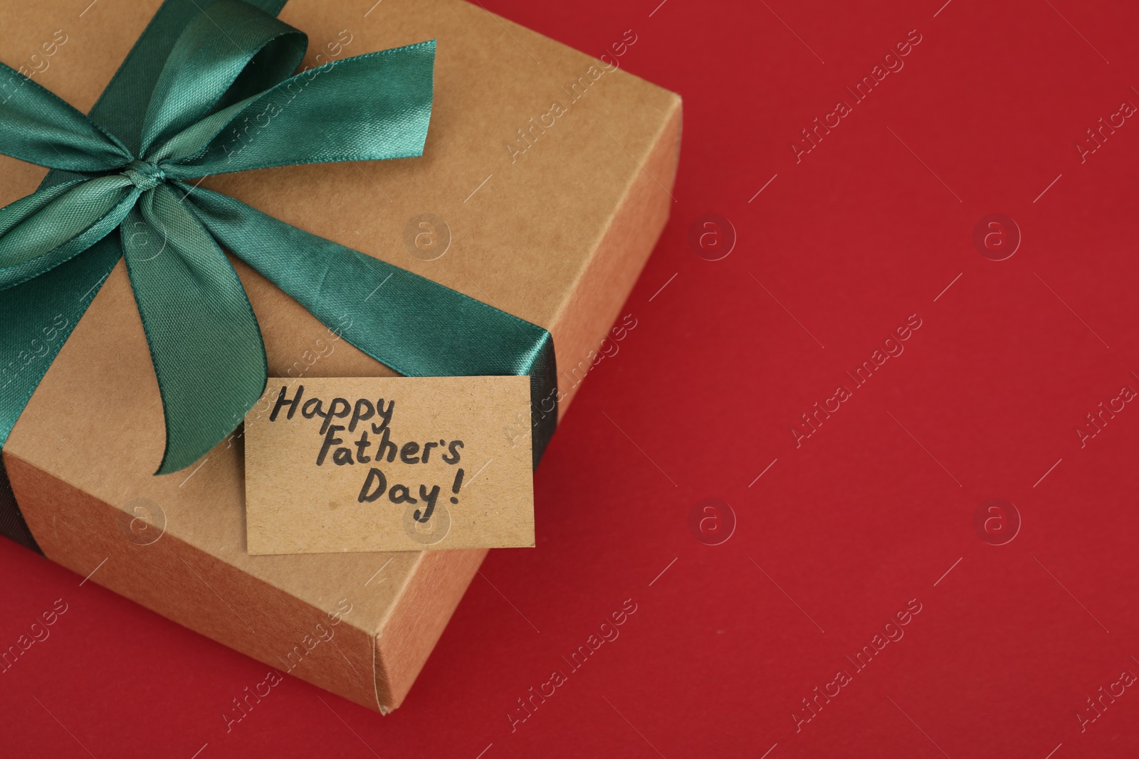 Photo of Happy Father's Day. Gift box and card with greetings on red background, closeup. Space for text