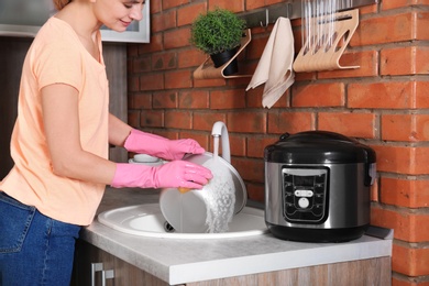 Woman washing modern multi cooker in kitchen sink