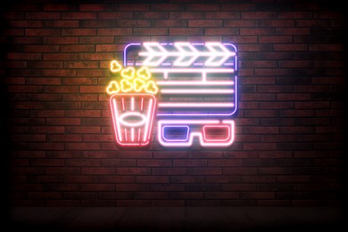 Glowing neon sign with popcorn bucket, clapper and glasses on brick wall