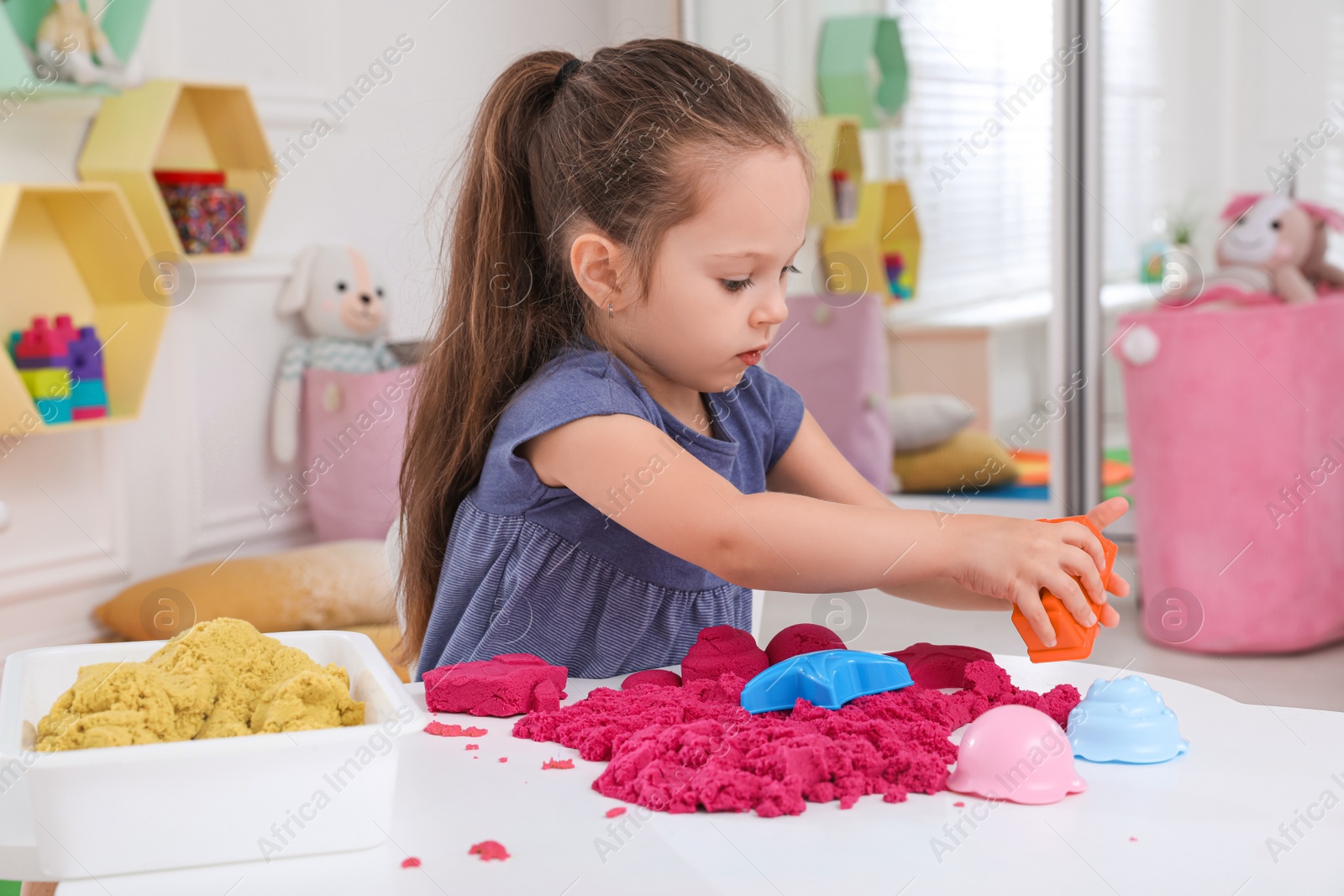 Photo of Cute little girl playing with bright kinetic sand at table in room