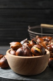 Photo of Delicious roasted edible chestnuts in wooden bowl on grey marble board, closeup