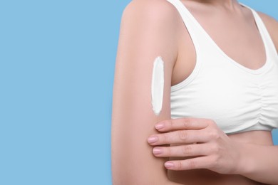 Photo of Woman with smear of body cream on her arm against light blue background, closeup. Space for text