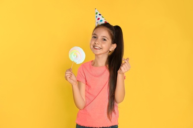 Happy girl with candy on yellow background. Birthday celebration