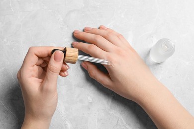 Woman dripping serum from pipette on her hand at light grey marble table, top view