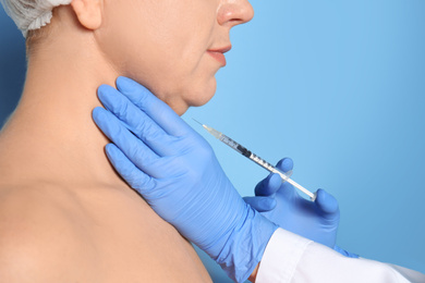 Mature woman with double chin receiving injection on blue background, closeup
