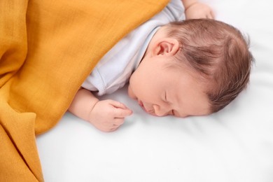 Cute newborn baby sleeping under orange blanket on bed