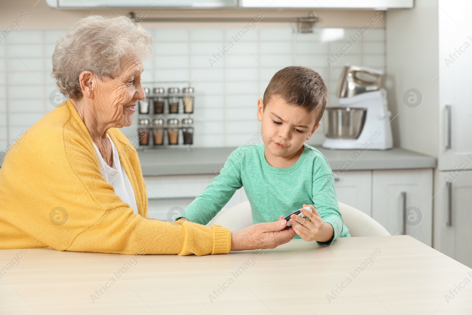 Photo of Senior woman with her grandson using digital glucometer at home. Diabetes control