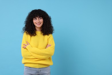Happy young woman in stylish yellow sweater on light blue background, space for text