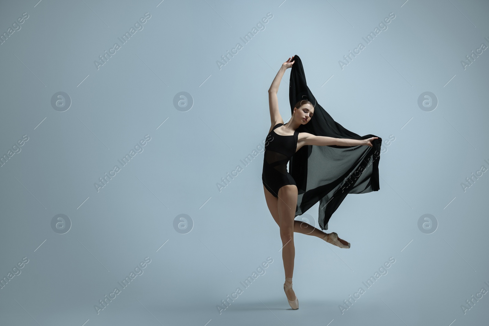 Photo of Graceful young ballerina practicing dance moves with black veil on grey background. Space for text