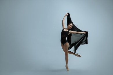 Graceful young ballerina practicing dance moves with black veil on grey background. Space for text