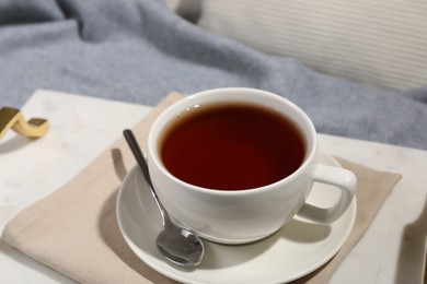 Aromatic tea in cup, saucer and spoon on table, closeup
