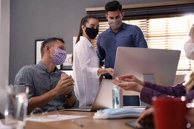 Photo of Group of coworkers with protective masks in office. Business meeting during COVID-19 pandemic