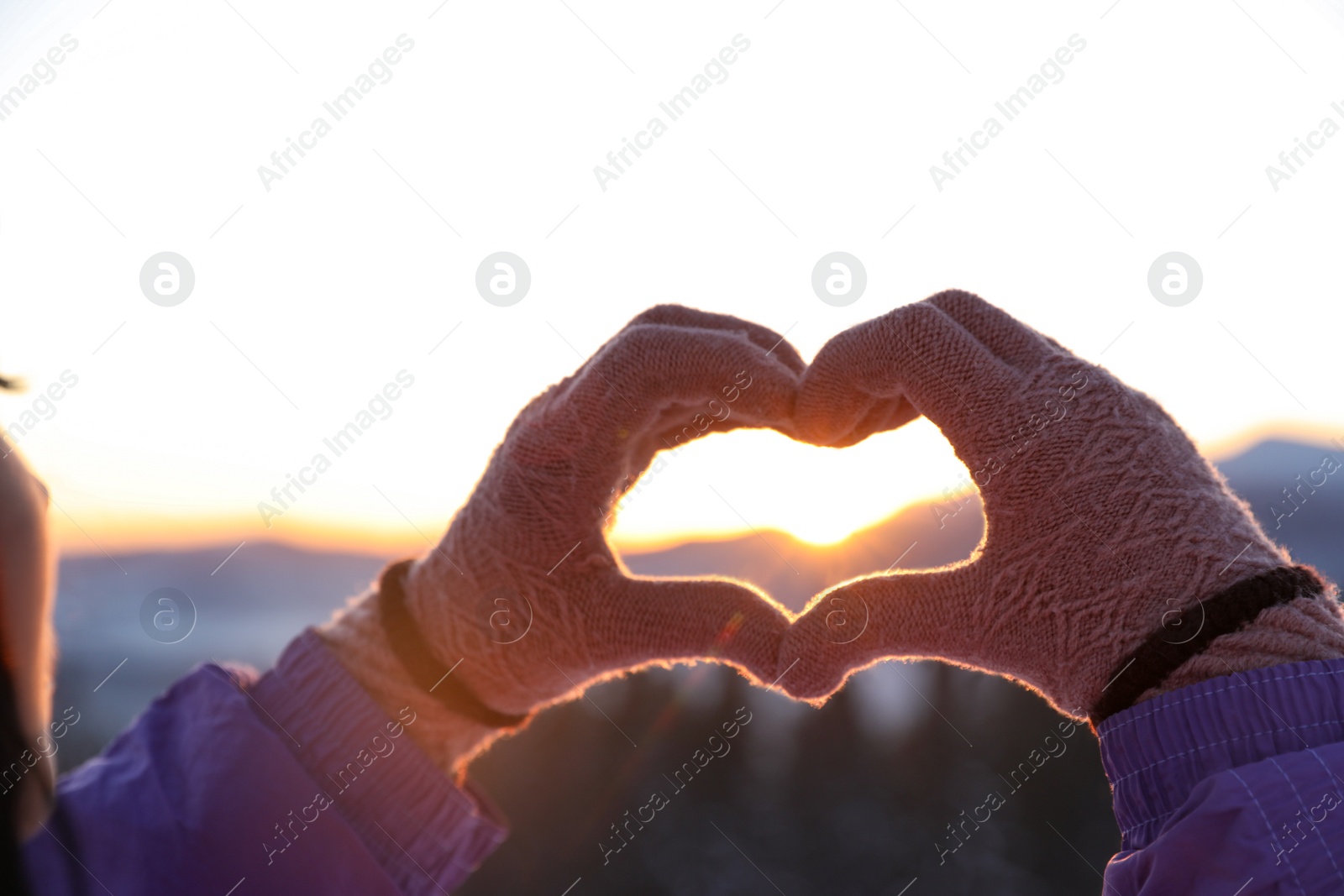 Photo of Woman making heart with her hands in mountains at sunset, closeup. Winter vacation