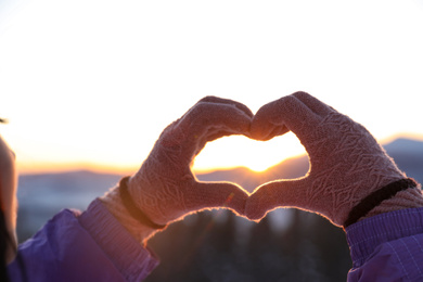 Woman making heart with her hands in mountains at sunset, closeup. Winter vacation