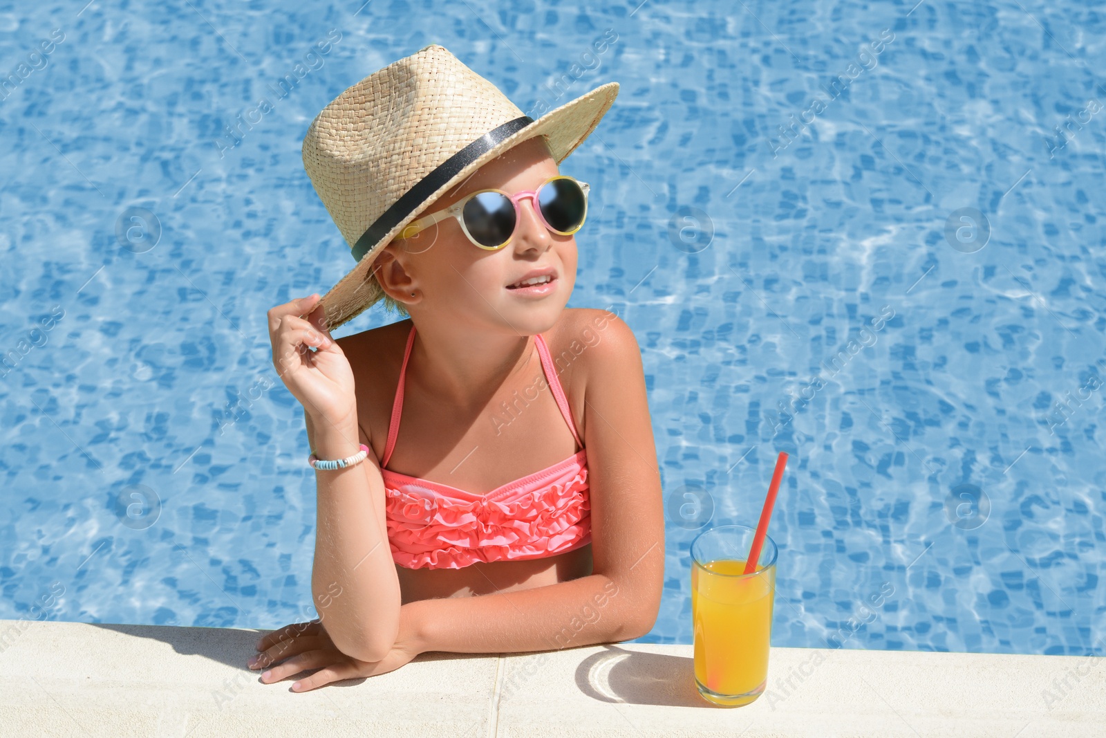 Photo of Cute little girl with glass of juice in swimming pool on sunny day