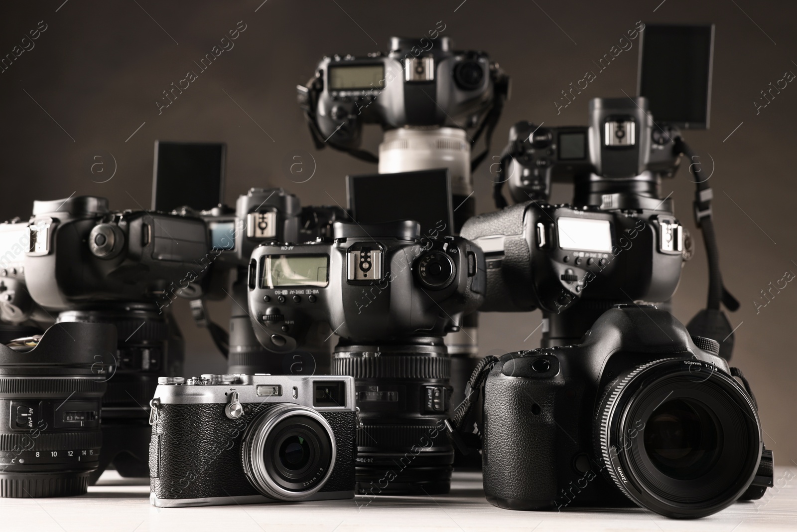 Photo of Modern cameras on white table against dark background, closeup