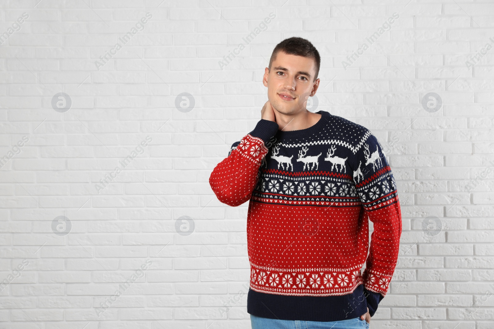 Photo of Portrait of young man in Christmas sweater near white brick wall. Space for text