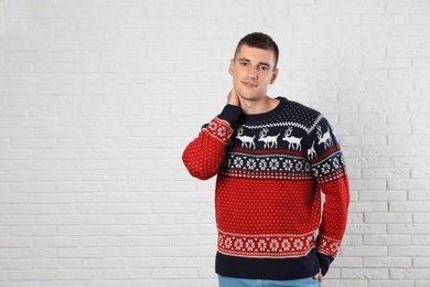 Photo of Portrait of young man in Christmas sweater near white brick wall. Space for text