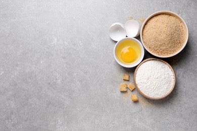 Fresh breadcrumbs, flour and egg on light grey table, flat lay. Space for text