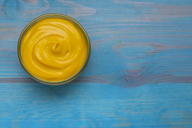 Photo of Sauce bowl with delicious mustard on light blue wooden table, top view. Space for text