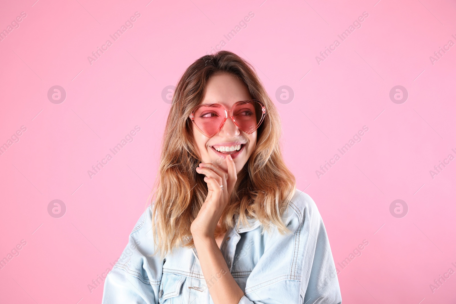 Photo of Young beautiful woman wearing heart shaped glasses on pink background