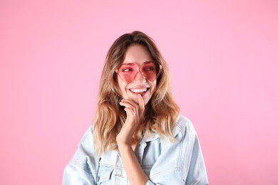 Young beautiful woman wearing heart shaped glasses on pink background