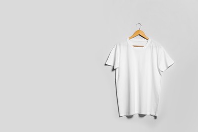 Hanger with white t-shirt on light wall. Mockup for design