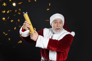 Emotional man in Santa Claus costume blowing up party popper on black background