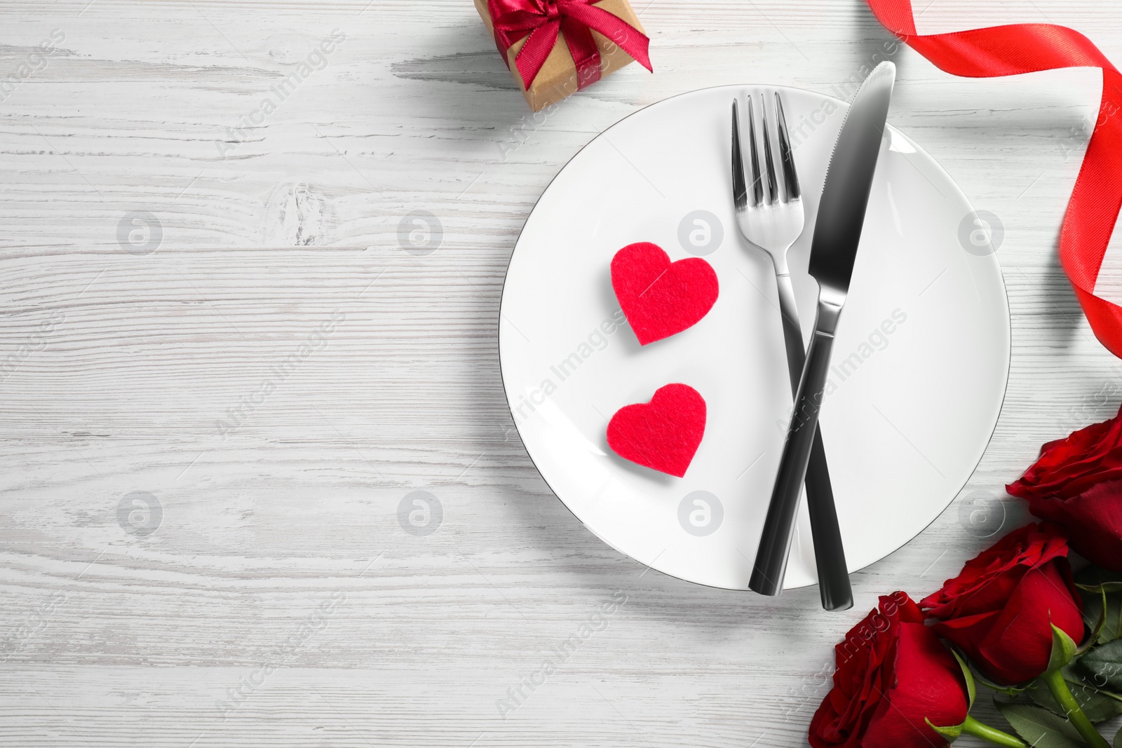 Photo of Beautiful place setting with dishware, gift and bouquet for romantic dinner on white wooden table, flat lay. Space for text