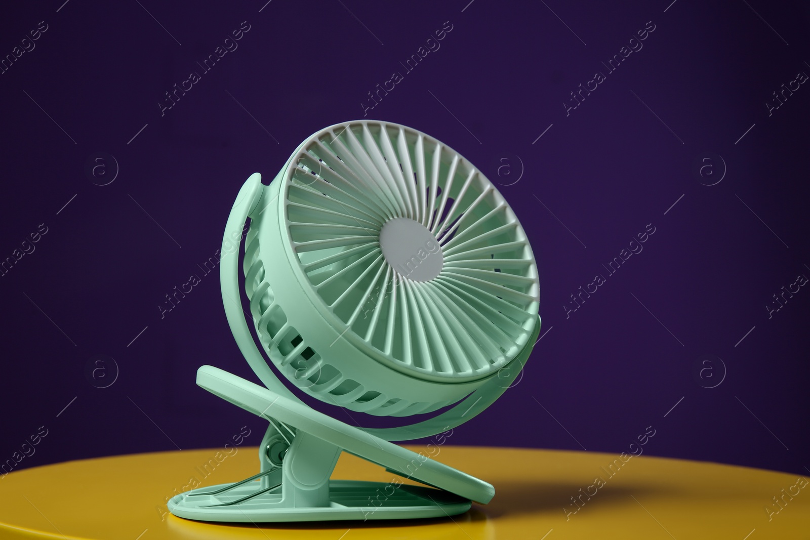 Photo of Modern electric fan on yellow table against violet background